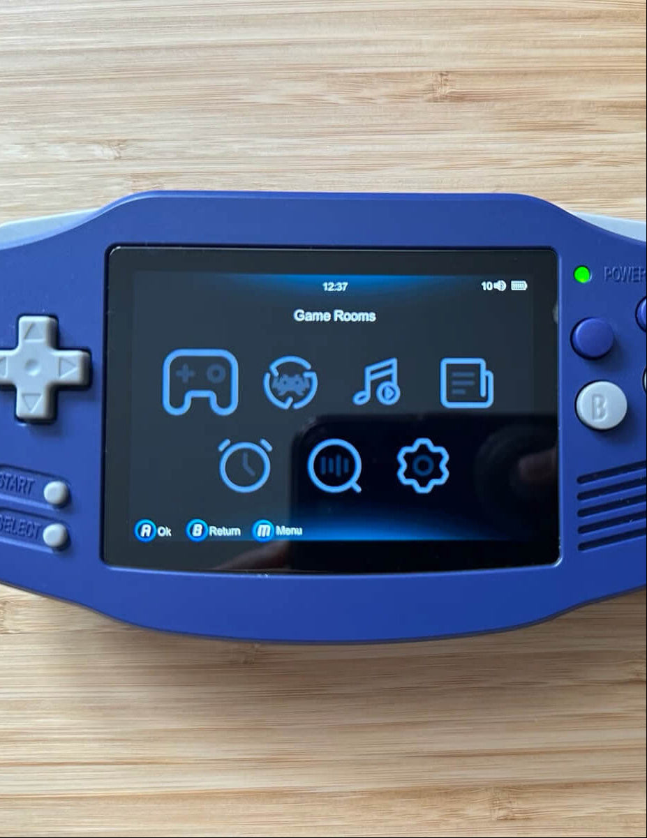 Blue handheld gaming device with screen displaying icons on a wooden surface, accompanied by a black cable.