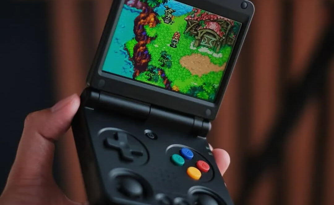 Hand holding a portable gaming device with a colorful game displayed on the screen.