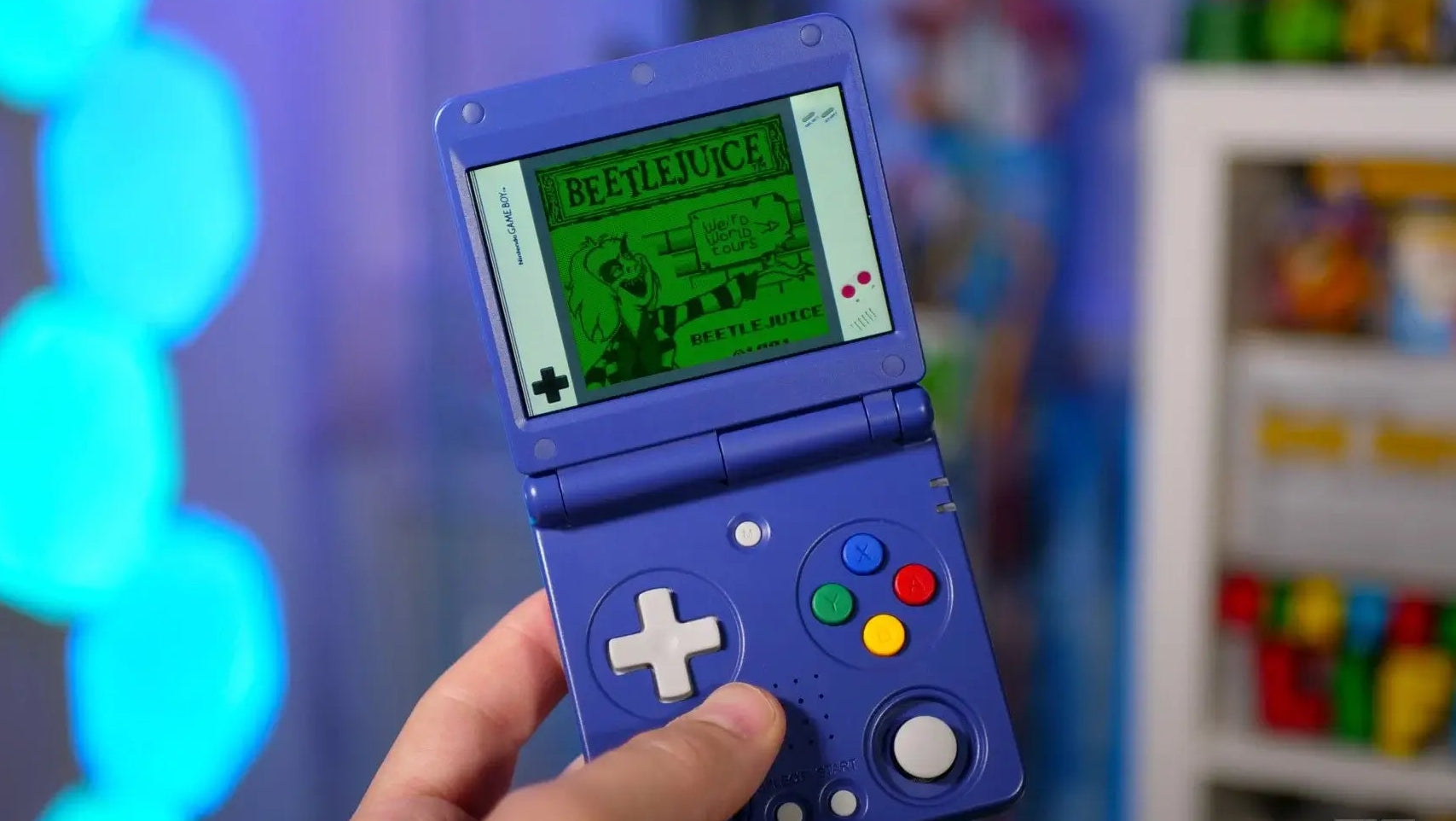 Hand holding a blue handheld gaming device with a colorful screen displaying text.